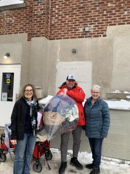 Two women and a man holding up a large bag of donated clothing